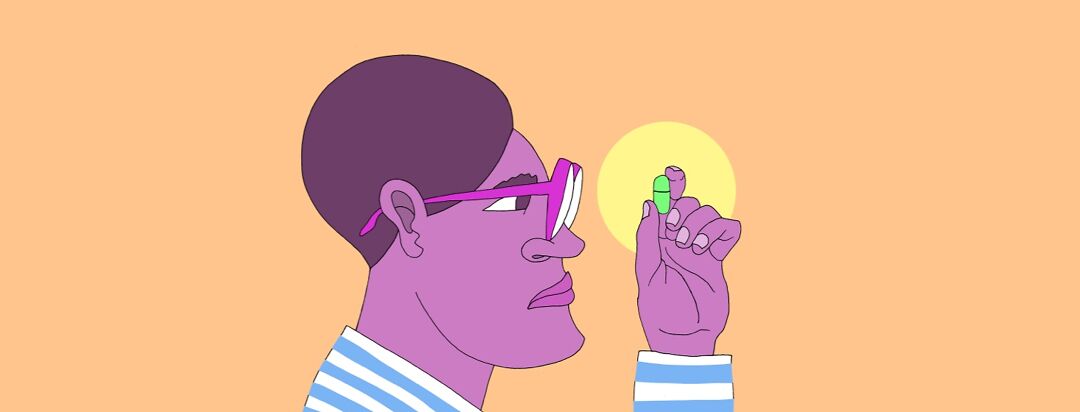 A man with glasses holding up a pill looking at it intensely